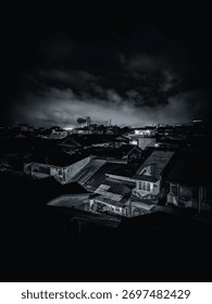 Atmospheric, dramatic nighttime view over densely packed city rooftops with corrugated metal, illuminated by streetlights that cast an eerie glow on the thick, cloudy sky above the urban landscape