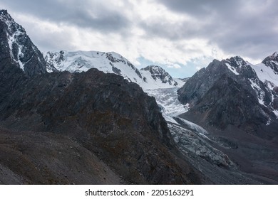 Atmospheric Landscape With Large Snow Mountain Range With Glacier And Icefall In Dramatic Cloudy Sky. Awesome High Snowy Mountains Under Rainy Clouds. White Snow On Black Rocks In Overcast Weather.