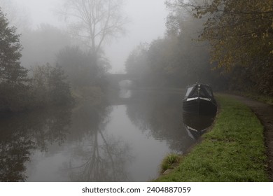 An atmospheric landscape looking down a canal. The image  was taken on a foggy morning, there is a narrow boat moored  and a bridge in the distance - Powered by Shutterstock