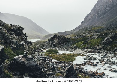 Atmospheric landscape with mountain lake and mountain creek among moraines in rainy weather. Bleak overcast scenery with milky river and lake among rocks. Gloomy view to milk mountain river and lake. - Shutterstock ID 2018906273