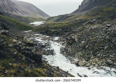 Atmospheric landscape with mountain lake and mountain creek among moraines in rainy weather. Bleak overcast scenery with milky river and lake among rocks. Gloomy view to milk mountain river and lake. - Shutterstock ID 2065749299