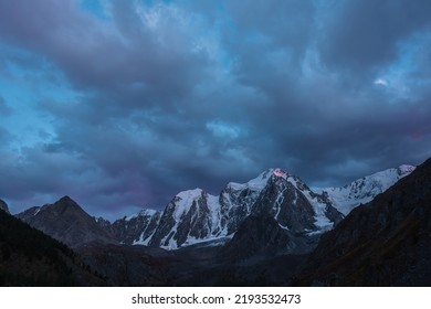 Atmospheric Landscape With Sunset Pink Reflection On Huge Snowy Mountain Top In Dramatic Sky. Scenic View To Giant Snow Mountains In Dusk. High Snow-covered Mountain Range Silhouettes In Twilight.