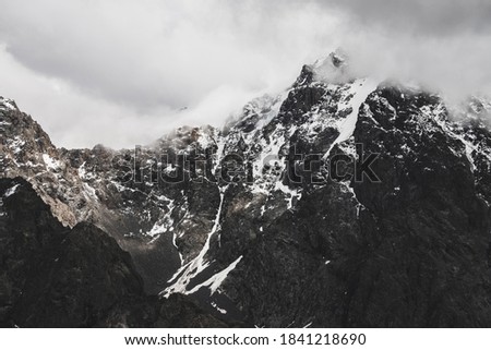 Atmospheric minimalist alpine landscape with snowy rocky mountain peak. Low clouds near snowbound range. Rocks with snow in mist. Craggy mountains in fog. Majestic misty foggy scenery on high altitude