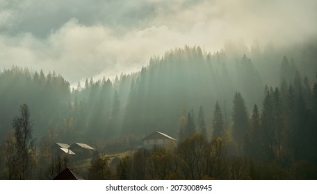 Atmospheric misty landscape of mountain village at autumn. Cloudy dramatic sky with sun rays over forest