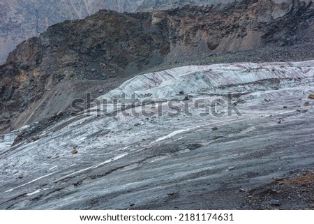 Atmospheric mountain landscape with long glacier tongue with crevasse and icefall close-up. Natural texture with orange stones on cracked glacial ice. Nature background with beautiful glacier on rocks