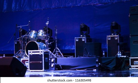 Atmsopheric background with a set of drums and speakers set up on a stage in blue light ready for a band to give a performance