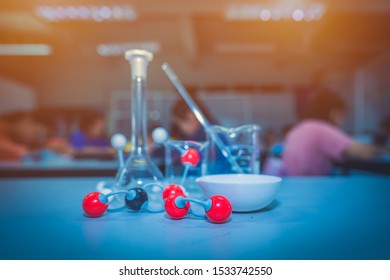 Atomic model and chemical science glassware on table in laboratory classroom, red black and white ball show chemical bonding atom, blurred beaker and flask, students learning and writing data in class - Powered by Shutterstock