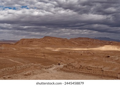 Atop Aït Benhaddou, a solitary figure contrasts the vast desert expanse under a brooding overcast sky. - Powered by Shutterstock