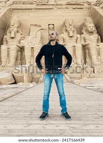 aTourist in front of the Colossal Statues of Ramesses II seated on a throne near the entrance to the Great Temple at Abu Simbel, Egypt