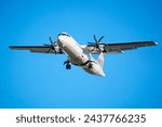 An ATR 72 airplane, a twin-engine turboprop short-haul regional passenger aircraft. Landing airplane. Blue background.