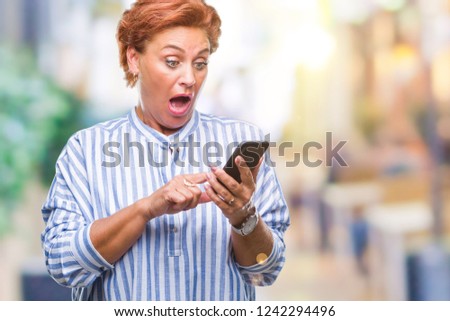Atrractive senior caucasian redhead woman texting using smartphone over isolated background scared in shock with a surprise face, afraid and excited with fear expression