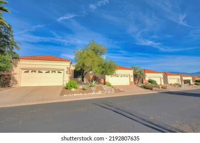 Attached Garages In A Subdivision At Tucson, Arizona. There Is An Asphalt Road With Cracks At The Front Of The Driveway With White Garage Doors And Concrete Tile Roofs Against The Blue Sky.