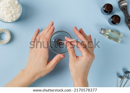 Attaching candle wick into a jar, candles making. Woman hand making candle. Flatlay, top view. Blue background