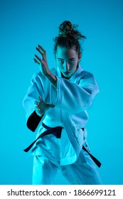 Attack. Professional Female Judoist In White Judo Kimono Practicing And Training Isolated On Blue Neoned Studio Background. Grace Of Motion And Action. Healthy Lifestyle, Sport Concept