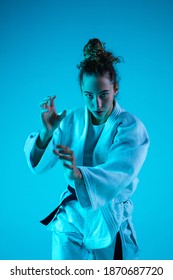 Attack. Professional Female Judoist In White Judo Kimono Practicing And Training Isolated On Blue Neoned Studio Background. Grace Of Motion And Action. Healthy Lifestyle, Sport Concept