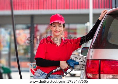 Attendant service female worker holding pipe nozzle refuelling car at gas station. Young assistant woman refuelling car at petrol station with happy, smile and wear red uniform and red hat