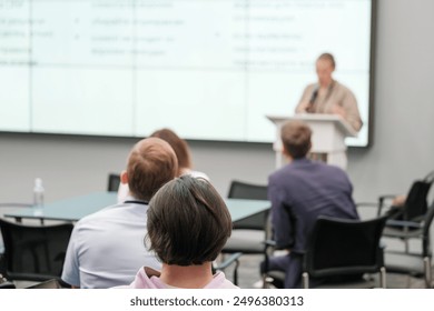 Attendees engaged with speaker presenting at a business conference or seminar in a modern office setting - Powered by Shutterstock