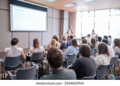 Attendees sit attentively as speaker presents during business conference. Bright, modern meeting room enhances learning experience while promoting collaboration and focus among participants.