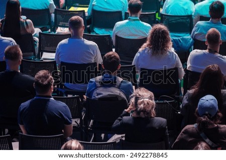 Attendees sit in rows facing forward at a conference, engrossed in the presentation on stage