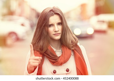 Attention! Closeup portrait head shot confident angry serious young girl business woman showing index finger for admonition isolated cityscape outdoor background. Multicultural mixt race asian russian