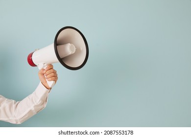 Attention please. Unknown man's hand on light blue background holds loudspeaker which is symbol of advertising, PR and promotion. Alert, announcement, warning and advertising concept. Copy space.