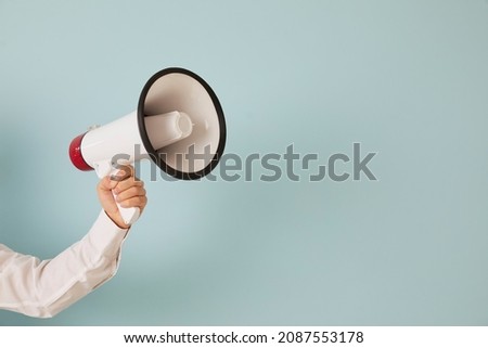 Attention please. Unknown man's hand on light blue background holds loudspeaker which is symbol of advertising, PR and promotion. Alert, announcement, warning and advertising concept. Copy space.