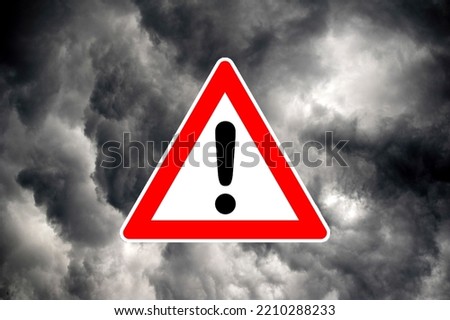 Attention warning sign in front of dramatic gray cloudy sky, symbolizing severe weather danger