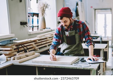 Attentive adult man marking up wooden board in contemporary workshop - Powered by Shutterstock