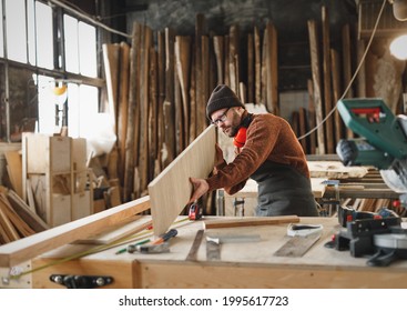 Attentive adult woodworker examining rasped wooden board while working in professional carpentry workshop