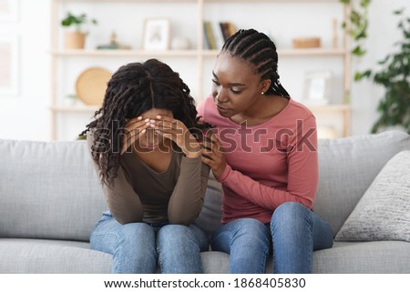 Attentive african american lady comforting her upset crying girlfriend or sister, giving her hug, saying supportive words, living room interior, copy space. Support in friendship concept