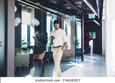 Attentive African American man in formal wear surfing smartphone and strolling along lobby with glass wall of modern office building - Powered by Shutterstock