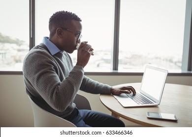 Attentive executive drinking coffee while using laptop in office