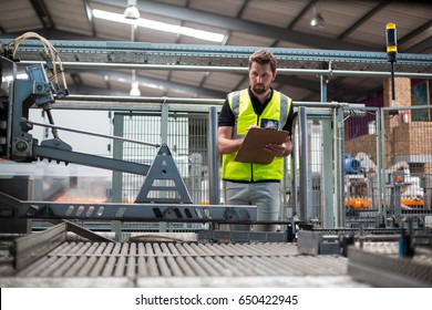 Attentive factory worker maintaining record on clipboard in factory - Powered by Shutterstock