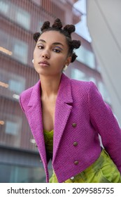 Attentive Fashionable Woman With Bun Hairstyle Looks Seriously At Camera Dressed In Stylish Pink Jacket Poses Against City Background Has Bright Vivid Makeup. People Style And Fashion Concept