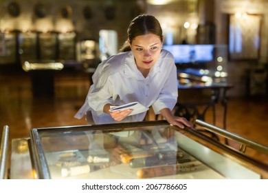 Attentive Girl Visitor At Museum Looks At Exposition Behind A Glass Display Case