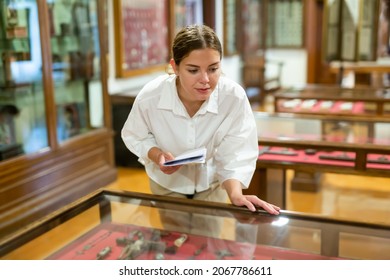 Attentive Girl Visitor At Museum Looks At Exposition Behind A Glass Display Case