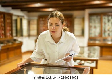 Attentive Girl Visitor At Museum Looks At Exposition Behind A Glass Display Case