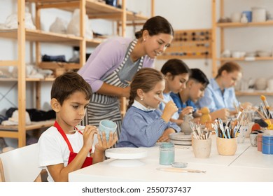 Attentive little boy painting handmade ceramic cup with brush in pottery workshop - Powered by Shutterstock