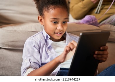Attentive little child girl playing at the tablet while sitting at the floor and relaxing
