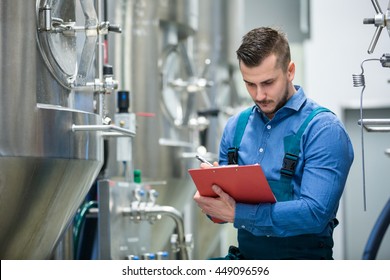 Attentive maintainance worker writing on clipboard at brewery - Powered by Shutterstock