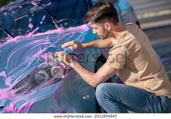 Attentive man washing car\
with pink foam