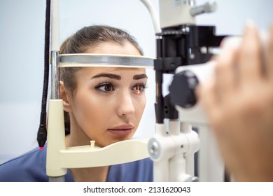 Attentive optometrist examining female patient on slit lamp in ophthalmology clinic. Young beautiful woman is diagnosed with eye pressure on special ophthalmological equipment. - Shutterstock ID 2131620043
