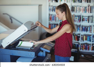 Attentive schoolgirl using Xerox photocopier in library at school - Powered by Shutterstock