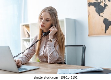 Attentive Travel Agent Talking On Phone And Using Laptop At Workplace