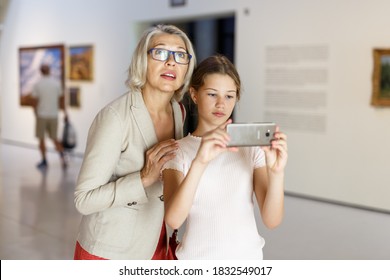 Attentive Tween Girl And Senior Woman Using Phone For Search Info About Painting In Museum