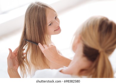 Attentive woman combing hair of her daughter