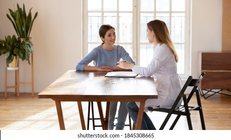 Attentive Woman Patient Sitting At Desk At Doctor Office Listening To Recommendations Of Female GP Or Counsel Of Psychologist, Medical Advisor Proposing Regular Insurance Policy To Interested Customer