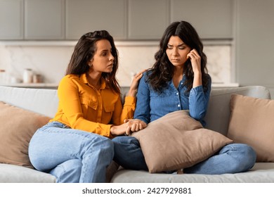 Attentive young woman comforting depressed friend or sister holding her hand, providing support to upset girlfriend in difficult life situation, helping cope with problems, sitting on couch indoor - Powered by Shutterstock