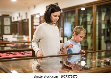 Attentive Young Woman With School Age Boy Exploring Artworks In Glass Case In Museum