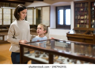 Attentive Young Woman With School Age Boy Exploring Artworks In Glass Case In Museum